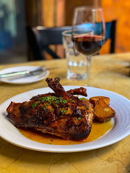 Best Asheville Restaurants Bouchon with roasted duck on plate with sauce and glass of water and red wine