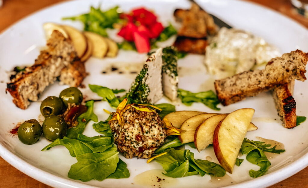 Featured article image for the best Asheville Restaurants with vegan cheese plate at Plant, which has a variety of nut-based cheeses, olives, and sliced apples with bread