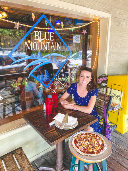 Blue Mountain Pizza Weaverville NC with white brunette woman in a blue dress sitting with a pizza in front of the restaurant