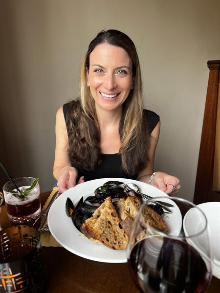 Christine, a white Brunette female in black top, eating a plate of mussels with bread at Bone and Broth Restaurant in Asheville, NC