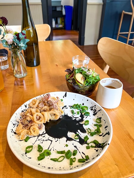 Fried calamari on a white plate with black sauce and green garnish next to tea cup and flower vase at ELDR Restaurant in Asheville, NC