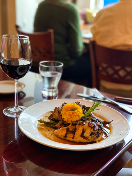 Glass Onion Weaverville Restaurant Near Asheville with chicken on plate in sauce with flower garnish and glass of red wine