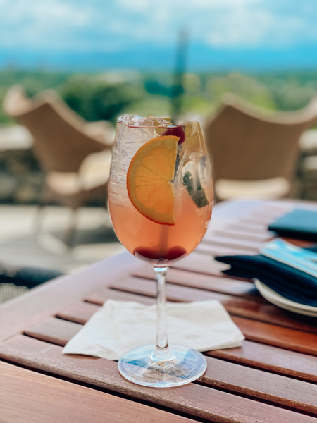 The Great Hall Bar Omni Grove Park Inn Asheville, NC white sangria cocktail with fruit garnish and blur of Blue Ridge Mountains and downtown Asheville in the background