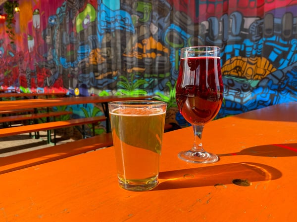 Yellow cider and amber beer on orange picnic table in shipping container structure with murals at Hi-Wire RAD Beer Garden in Asheville, NC