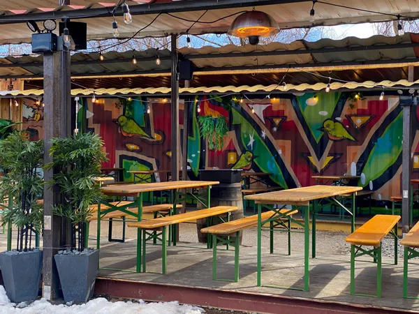 Hi Wire RAD Beer Garden with colorful bird mural along shipping container inside and brown picnic tables