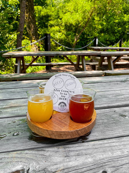 Hillman Beer Asheville Biltmore Village with flight of beer on picnic outside with trees and more picnic tables