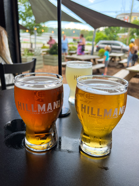 Hillman Beer Asheville NC Brewery with amber beer and yellow cider on black table top overlooking front patio