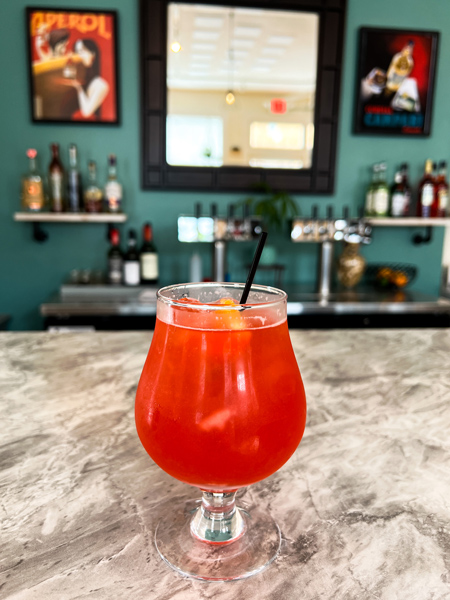 Hoppy Trees Beer Spritz Bar Weaverville North Carolina with orange spritz cocktail sitting on gray marble bar with liquor in background on shelves with mirror and pictures