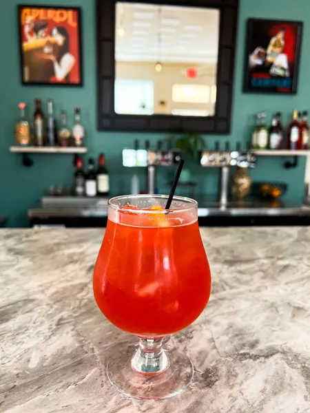 Hoppy Trees Beer Spritz Bar Weaverville North Carolina with orange spritz cocktail sitting on gray marble bar with liquor in background on shelves with mirror and pictures
