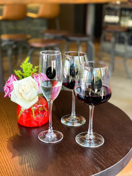 Marked Tree Vineyard Wine Bar Asheville NC with two red glasses of wine and Champagne flute with vase of flowers on table