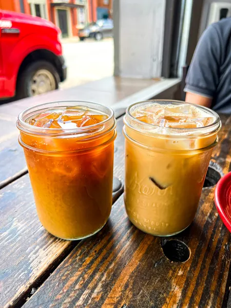 Odd's Cafe Coffee in Asheville NC with dark and lighter ice coffees in mason jars on wooden brown table by open window with red car in the background