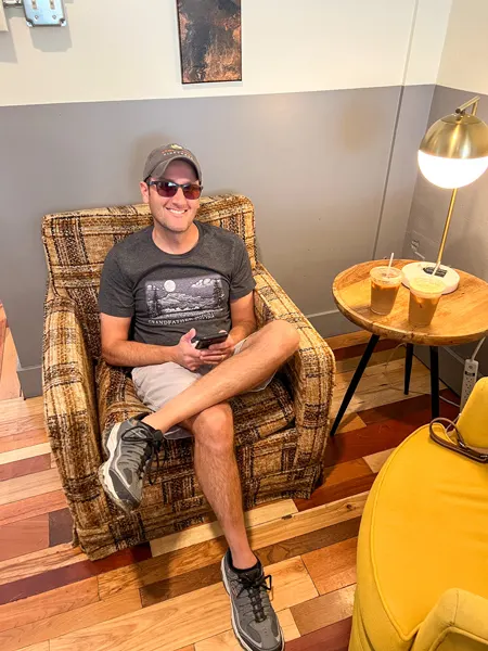 PennyCup Coffee Asheville NC Shop with white brunette male with sunglasses and hat wearing t-shirt and shorts sitting in a plaid chair next to table with ice coffees