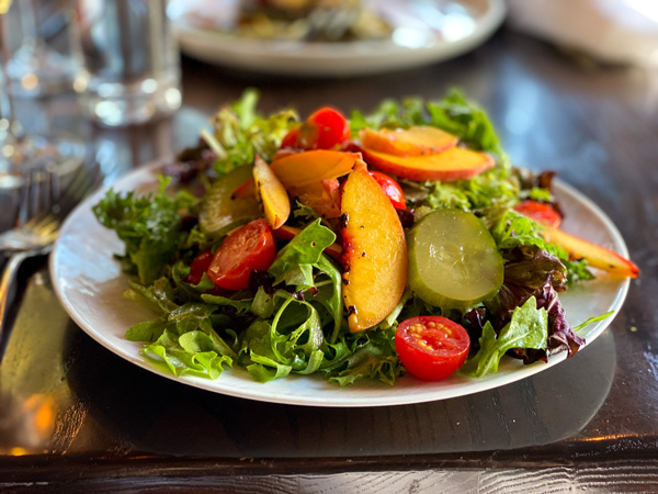 Posana Restaurant Downtown Asheville with plate of salad with lettuce, peaches, cucumbers, and tomatoes