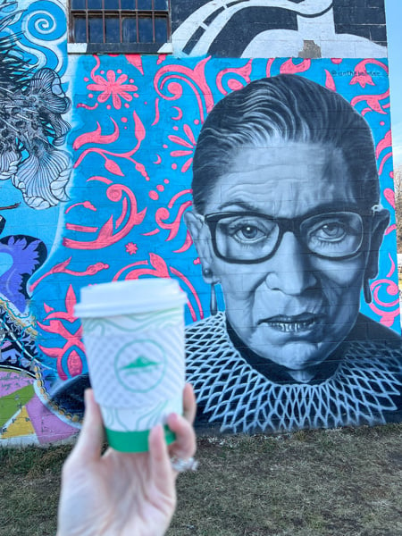 RGB Mural outside Summit Coffee in Asheville NC with white hand holding up to-go Summit coffee cup in front of mural