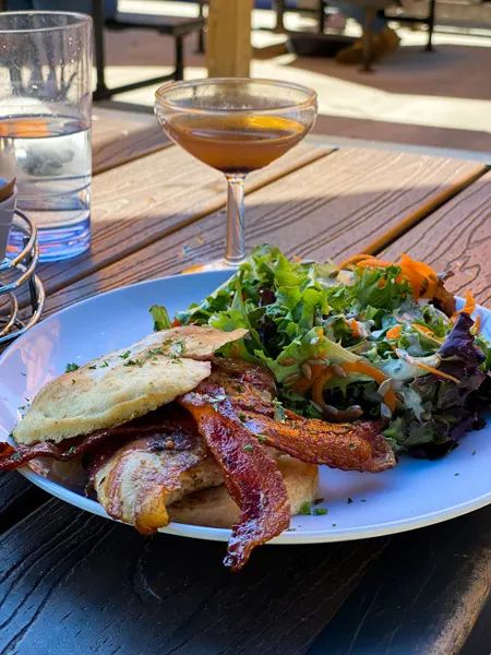 Sunny Point Cafe West Asheville brunch and lunch with gluten free chicken sandwich with bacon on plate with cocktail in background