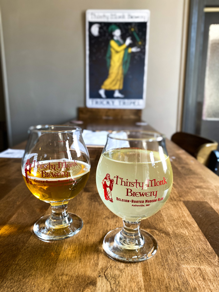 Thirsty Monk Brewery Asheville NC with yellow cider and half pour lager on brown table with wall decoration blurred in background