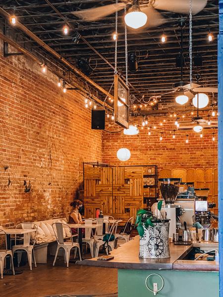 Trade and Lore Coffee Downtown Asheville NC with tall ceilings, hanging lights, tables, chairs, and coffee bar