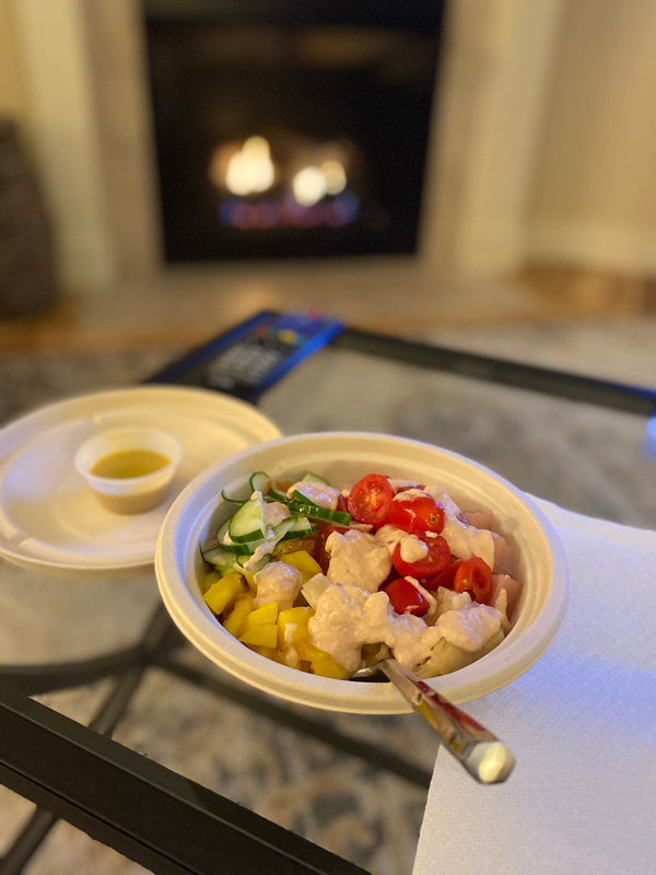 Yum Poke Bowl in Asheville, NC with tomatoes, white rice, sushi, cucumber, and mango in takeaway bowl in front of blazing fireplace