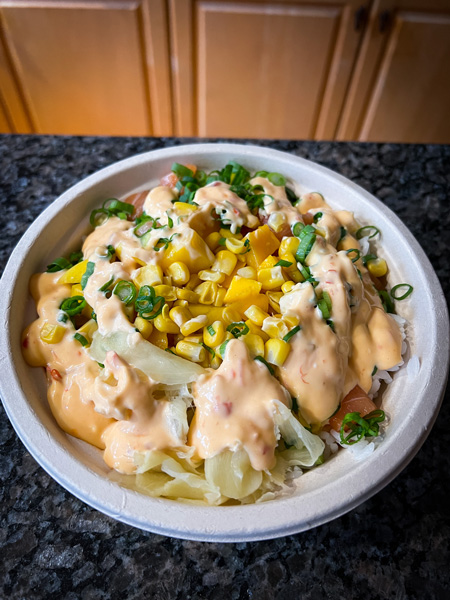 Yum Poke Spot Takeout Sushi in Asheville NC with take away bowl filled with white rice, ginger sauce, sweet corn, raw salmon, and cilantro