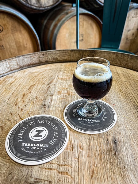 Zebulon Artisan Ales Brewery Weaverville NC with two coasters with logo and half pour of craft brown colored beer on wine barrel table top