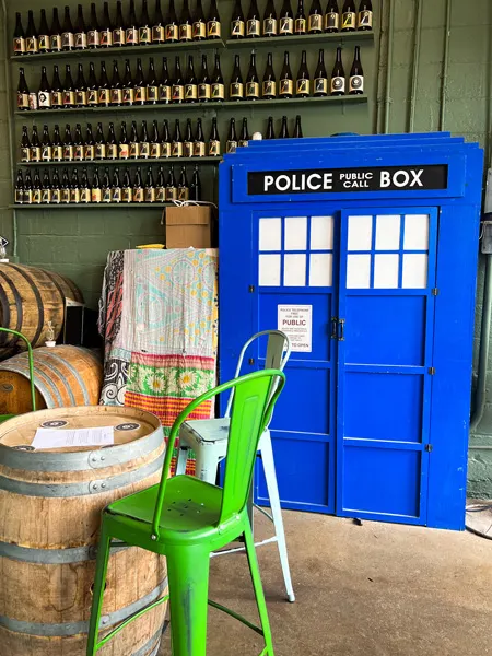 Zebulon Artisan Ales Weaverville NC with green and silver chairs around wine barrel table top with blue police box Dr. Who TARDIS against wall lined with beer bottles