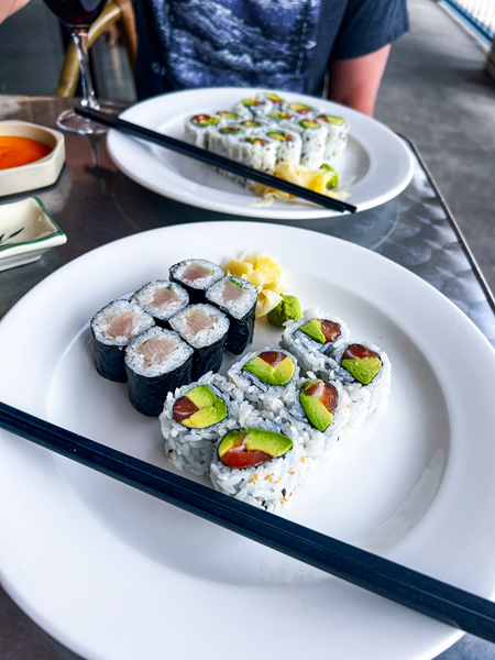 Zen Sushi in Asheville NC Lunch Rolls with six tuna and avocado and six yellow tail and scallion sushi rolls on white plate with black chopsticks and second sushi roll plate blurred in background on outdoor dining table