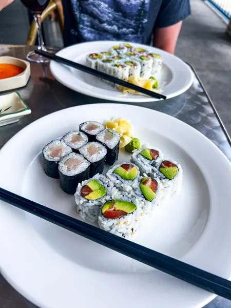 Zen Sushi in Asheville NC Lunch Rolls with six tuna and avocado and six yellow tail and scallion sushi rolls on white plate with black chopsticks and second sushi roll plate blurred in background on outdoor dining table
