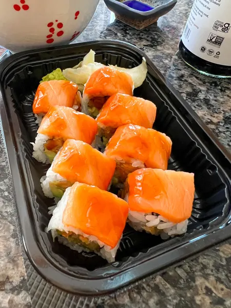 Zen Sushi Asheville NC Takeout Rolls with 8 pieces topped with raw salmon and filled with more fish and avocado in takeaway container with wasabi and ginger