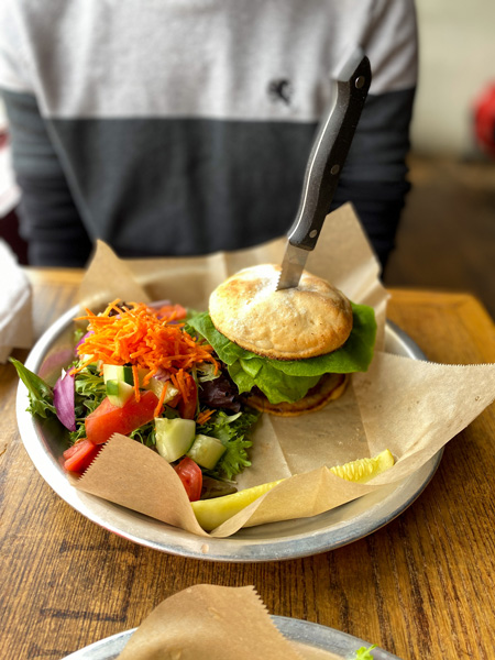 Burger The Trailhead Restaurant Black Mountain NC with knife in gluten-free burger bun and burger sitting next salad with lettuce, tomatoes, carrots, and red onion