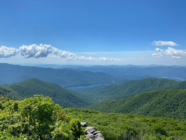 Craggy Pinnacle Hike Blue Ridge Parkway Asheville NC with view of Asheville watershed, stone wall, and blue sky with clouds