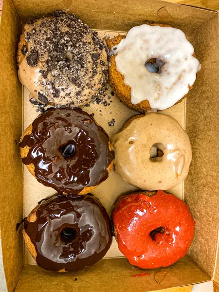 Dough House vegan donuts in Black Mountain NC with half dozen vegan and gluten-free donuts in brown to go box with vanilla, chocolate, and strawberry glazed donuts