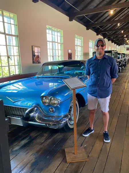 Estes-Winn Antique Car Museum in Asheville blue Eldorado Cadillac on wooden showroom floor with white male wearing hat and blue shirt with cargo pants standing in front of it
