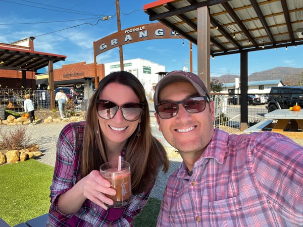 Tom and Christine, a white brunette male and female in pink plaid with sunglasses taking a selfie with craft cocktails at Foothills Grange in Black Mountain, North Carolina