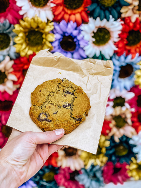 Gluten Free Desserts Asheville Old Europe Pastries with gluten-free and vegan chocolate chip cookie in front of colorful flowers