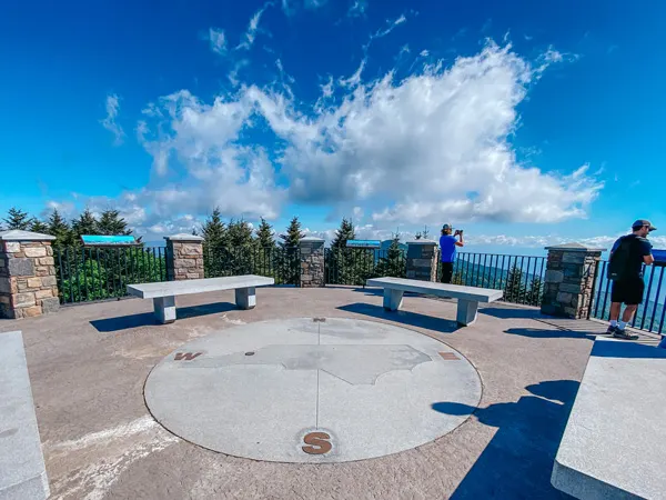 Mount Mitchell Summit Blue Ridge Parkway NC from viewing platform with compass on ground and view of mountains, blue sky, and white clouds