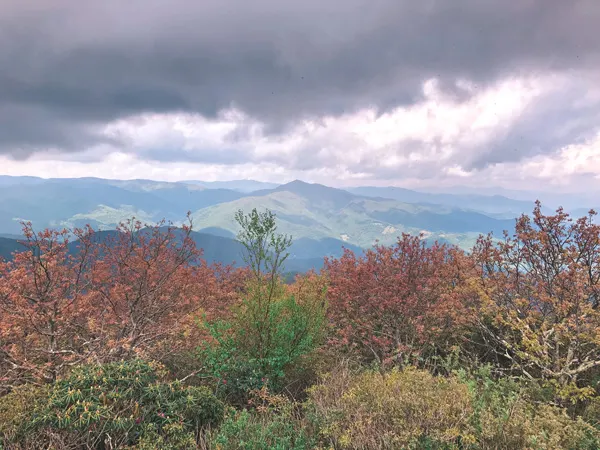 Mount Pisgah Blue Ridge Parkway Hikes NC with dark gray clouds over green and blue mountains with red and orange leaves