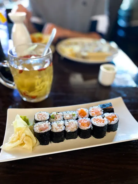 Soba Sushi Weaverville North Carolina restaurant with two full sushi rolls on a white plate with ginger and wasabi next to a glass of ginger tea and sake glass