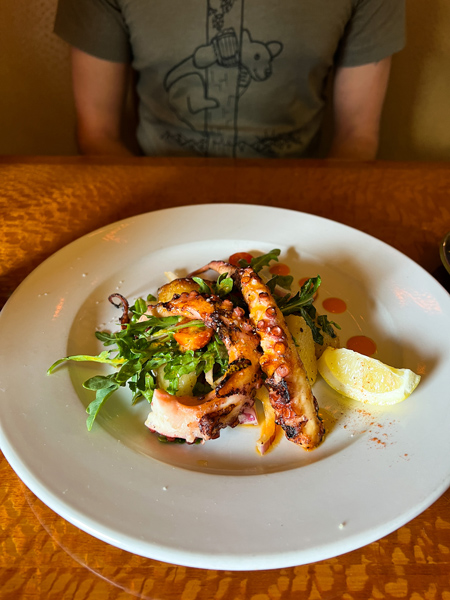 Stoney Knob Cafe Restaurant Weaverville Octopus with two legs on white plate with lemon, seafood salad, and roasted lemon potatoes