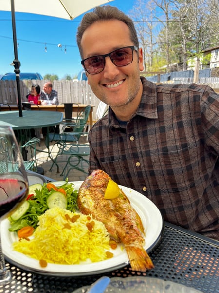 White brunette male in sunglasses eating full fish with yellow rice and salad at The Bush Farmhouse Restaurant in Black Mountain, NC