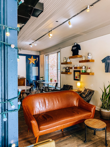 The Dripolator Coffeehouse Black Mountain NC with brown couch, hanging yellow lights, shelves lined with knick knacks, and blue wall with a star