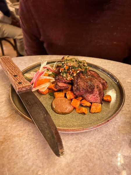Flat-iron steak on plate with vegetables and large steak knife at The Pure and Proper in Black Mountain, NC