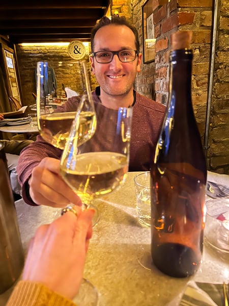 Tom, a white brunette male in maroon sweater doing a cheers with Christine with two glasses filled with white wine at The Pure and Proper Restaurant in Black Mountain, North Carolina