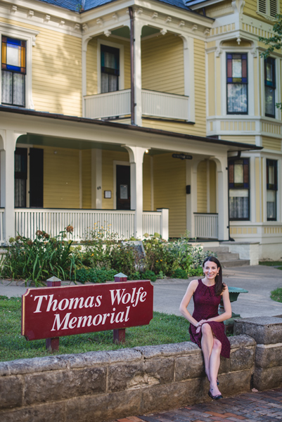 Thomas Wolfe Memorial Asheville Museums with brunette white woman in maroon dress sitting in front of yellow boarding house