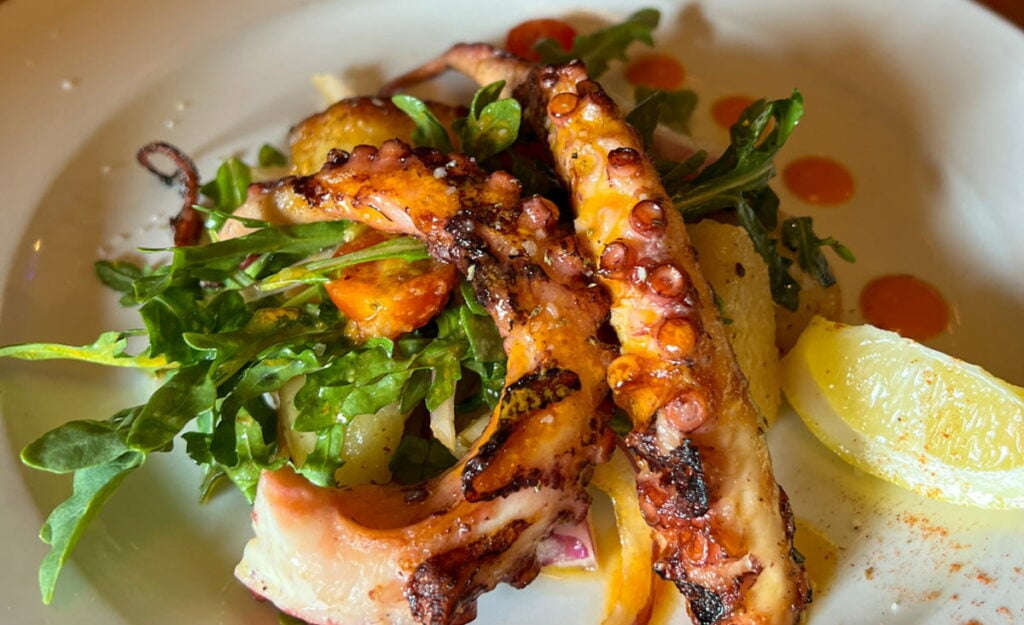 Weaverville Restaurants Guide featured image with close up of grilled Octopus with greens and lemon garnish on white plate from Stoney Knob Cafe