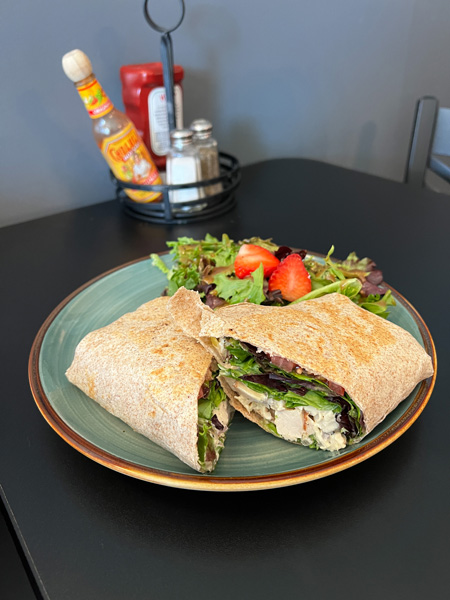 Chicken salad sandwich in a wrap with side salad on a plate on a black table from Yellow Mug Coffee Lounge in Weaverville NC