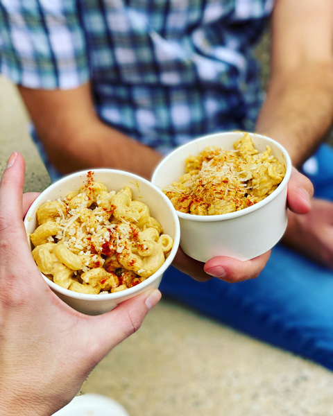 Asheville VeganFest Mac and Cheese with two takeaway containers of vegan mac and cheese with red seasoning