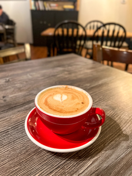 Black Bear Coffee Hendersonville NC with red cup filled with a latte on top of gray table with chairs and bookshelf blurred in background