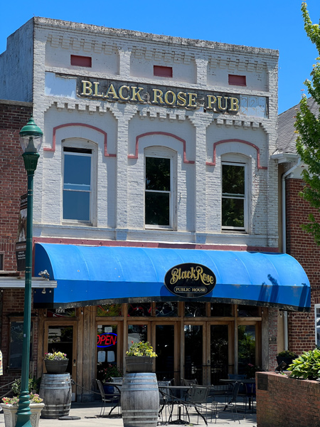 Black Rose Pub Hendersonville NC with historic white gray building facade with blue awning and tables out front