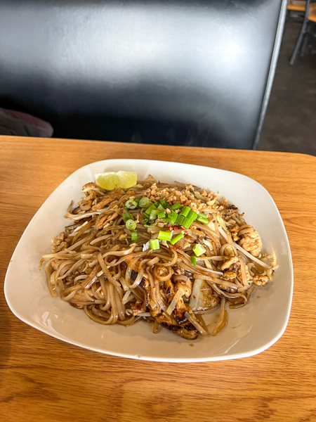 Boon Choo Thai Express Flat Rock NC GF Pad Thai on white plate on brown table with black booth chair and garnished with scallion and peanuts