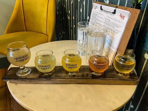 Botanist and Barrel Cidery in Asheville NC cider flight with 5 orange to yellow ciders on small table with menu in background